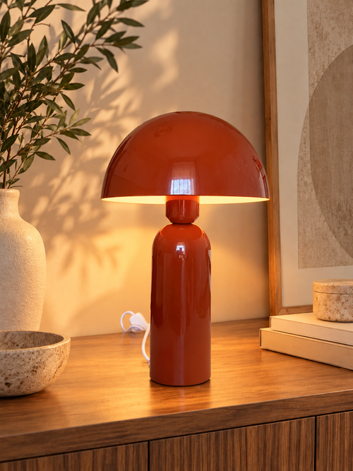 Lampe champignon paprika en métal allumée sur une console, créant une ambiance chaleureuse dans un intérieur.
